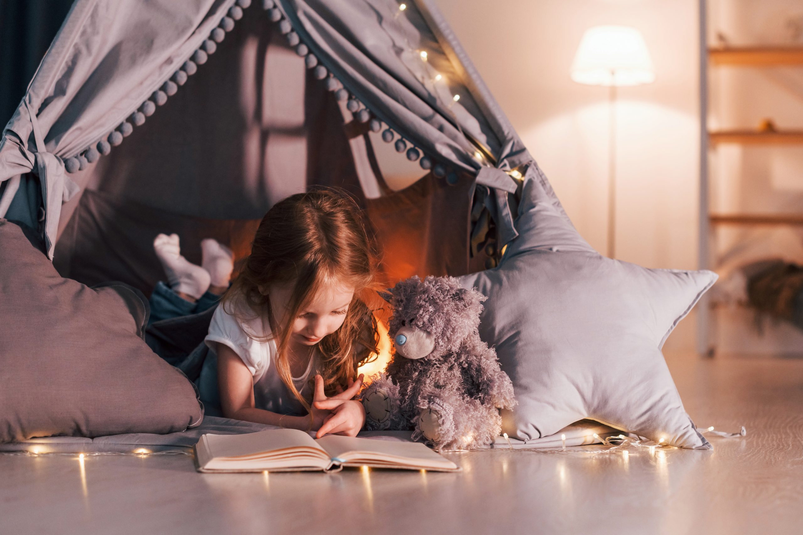 Reading the book. Cute little girl is in the tent in domestic room